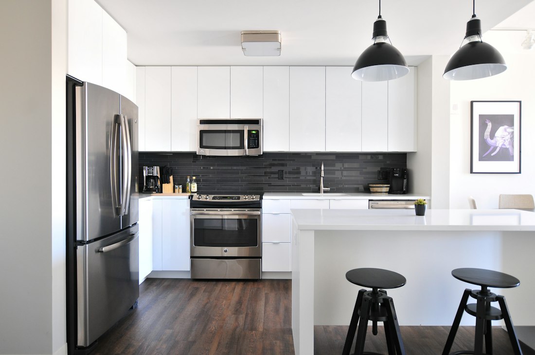 White kitchen with stainless-steel appliances, a dark tiled backsplash and an island with two black stools