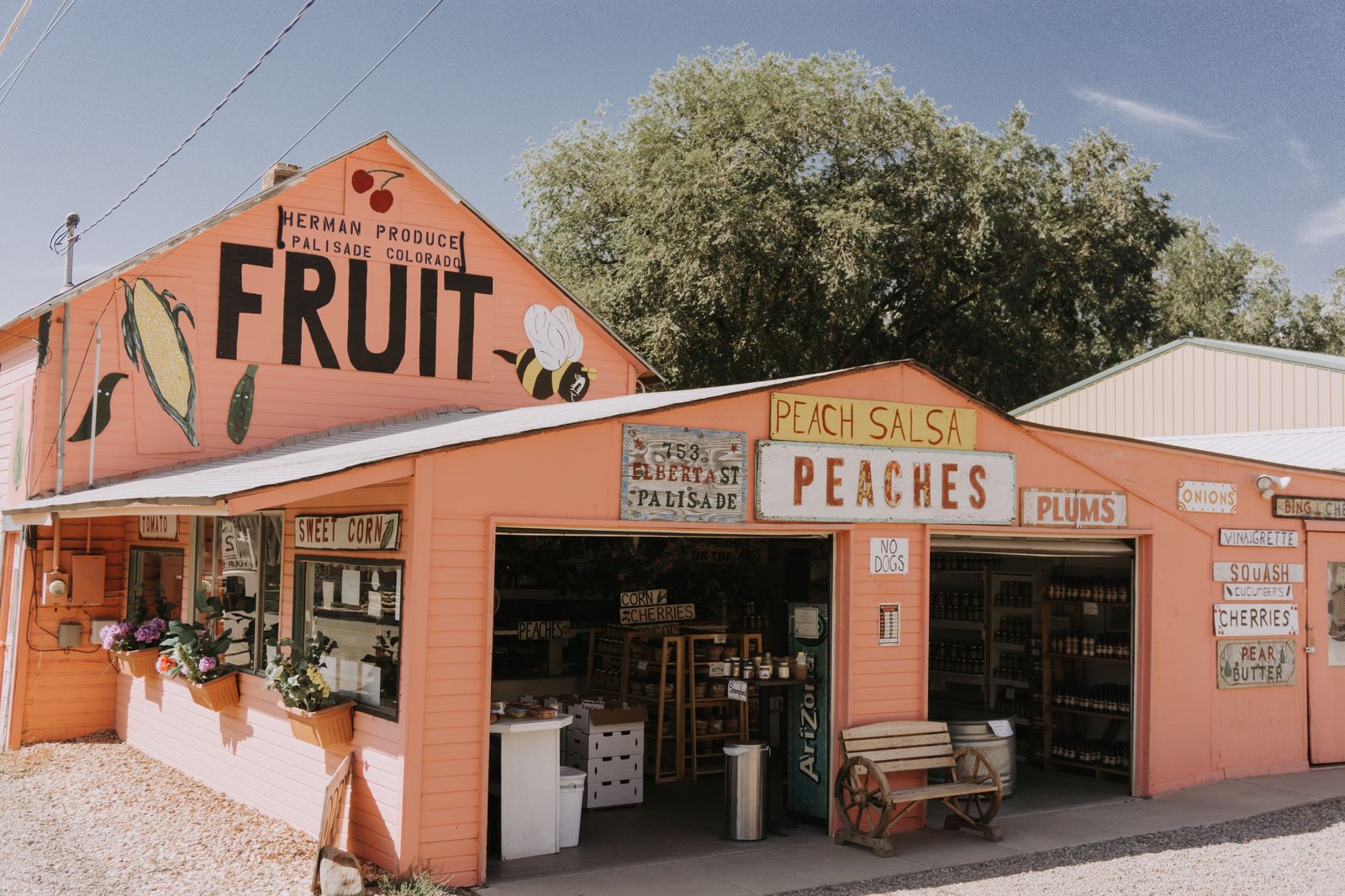 A pink roadside produce stand with hand-painted signs for fruit, peaches and plums