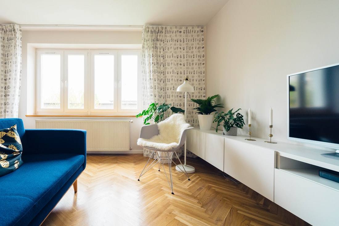 A bright living room with a blue sofa and a TV on a low white cabinet