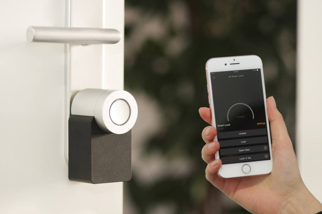 A phone running a smart-lock app, held beside a front door lock