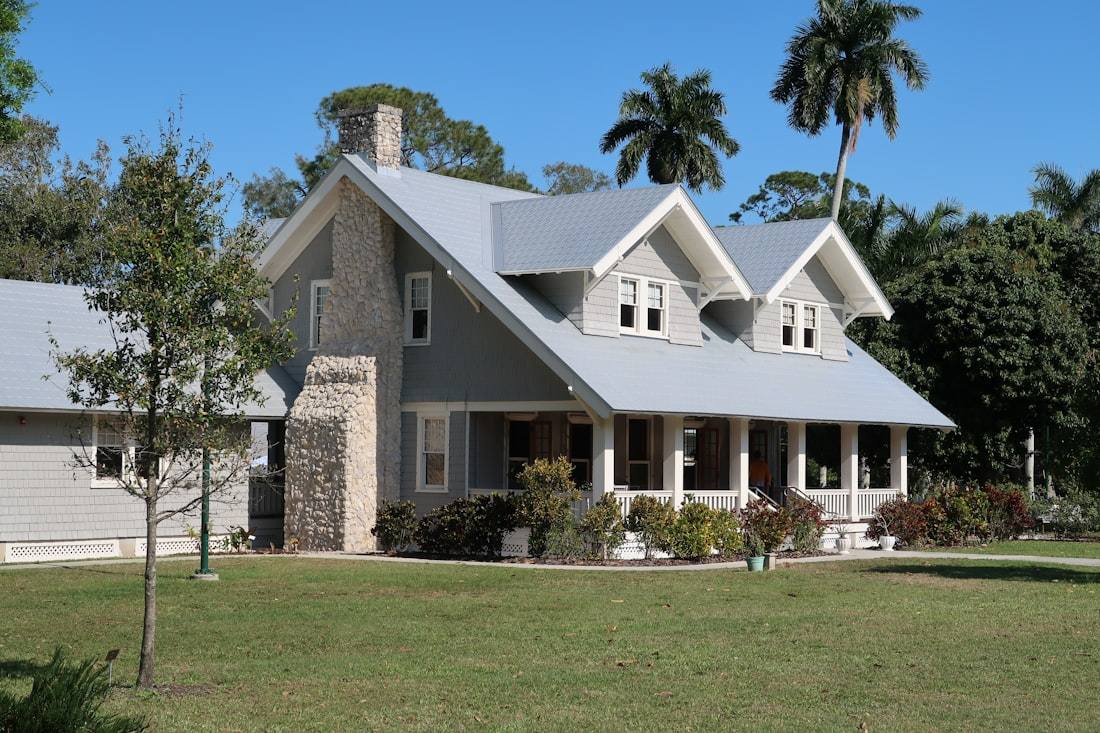 A gray craftsman house with a stone chimney and palm trees