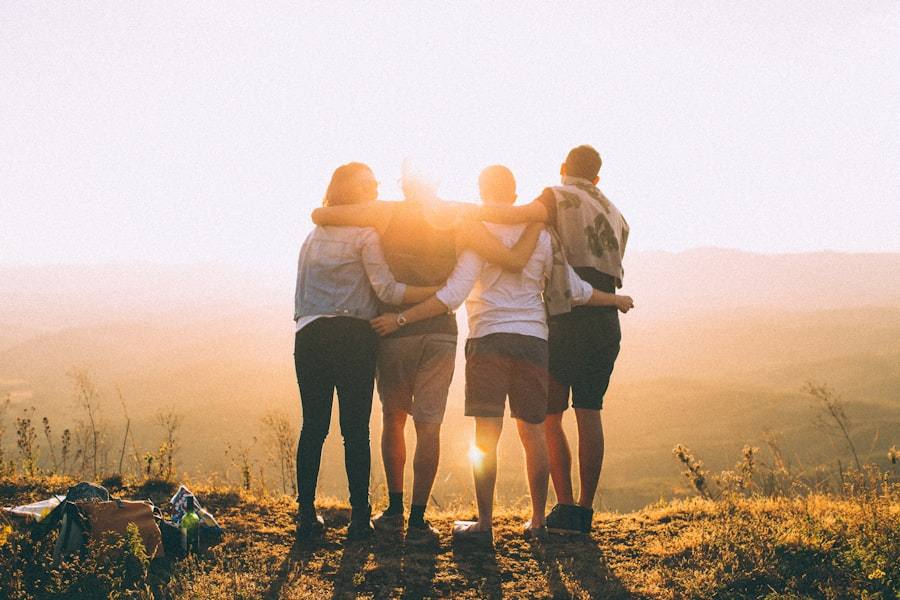 Four friends with arms around each other watching a sunset over hills