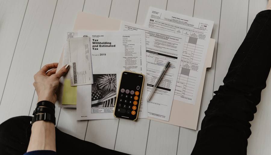 Tax forms, a phone calculator and a pen spread on a white floor